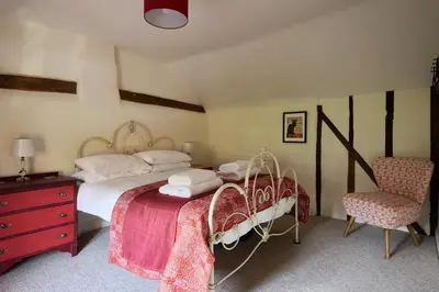 a bedroom with a bed with a red dresser and a chair at Church Cottage in Halesworth