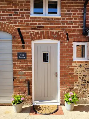 a brick house with a white door and two plants at Entire 2 bed coach house in peaceful Norfolk village in Pulham