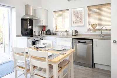 a kitchen with a wooden table and white cabinets at Hedgehog Cottage in Bury Saint Edmunds