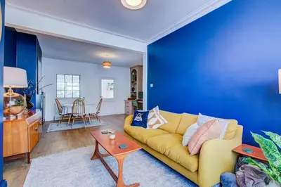 a living room with a yellow couch and a blue wall at Cosy house on the seafront - Pass the Keys in Southend-on-Sea