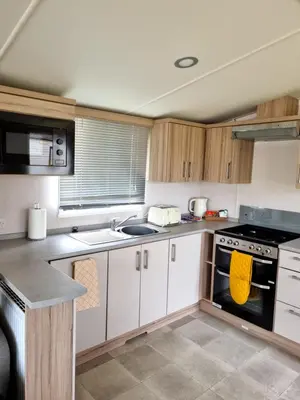 a kitchen with white cabinets and a stove top oven at Modern Family Caravan with WiFi at Valley Farm, Clacton-on-Sea in Great Clacton