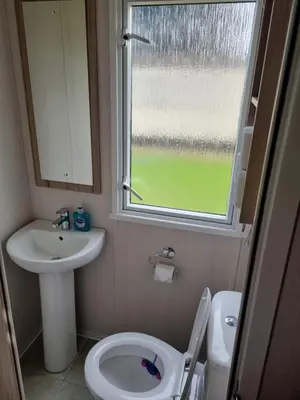 a bathroom with a toilet and a sink and a window at Modern Family Caravan with WiFi at Valley Farm, Clacton-on-Sea in Great Clacton