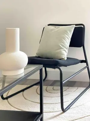 a chair with a pillow next to a table with a vase at Modern flat near train station with free parking in Cambridge