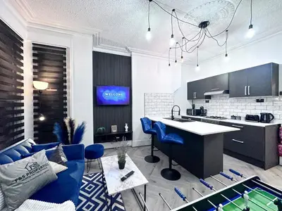 a living room with a blue couch and a kitchen at Swanky Seaside Sanctuary w foozeball - Southend in Southend-on-Sea