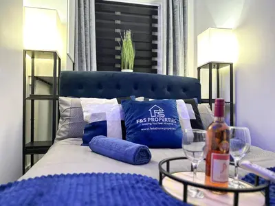 a bed with a blue headboard and a table with a bottle of wine at Swanky Seaside Sanctuary w foozeball - Southend in Southend-on-Sea