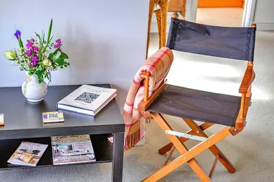 a rocking chair next to a table with a book at Finest Retreats - Kings Wharf - Luxury Riverside Home in Burnham on Crouch