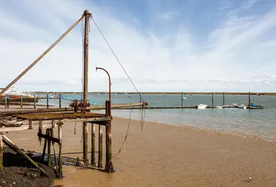 a dock on a beach with boats in the water at Finest Retreats - Kings Wharf - Luxury Riverside Home in Burnham on Crouch
