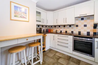 a kitchen with white cabinets and stools at 8 Saxonfields in Snape