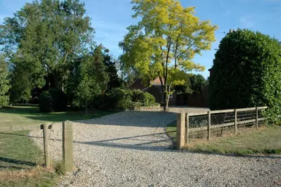 a wooden fence on a gravel road with trees at Field Cottage Bed and Breakfast in East Harling