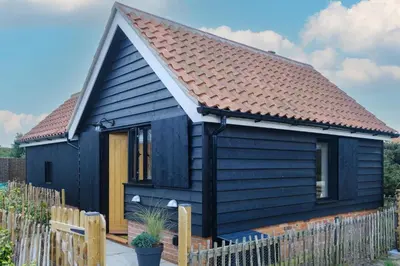 a black tiny house with a brown roof at Mission Lodge in Thorpeness