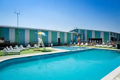 a pool with chairs and an umbrella in front of a building at Modern Caravan With Wifi At Seawick holiday park, Clacton on Sea 8 berth Large Decking in Clacton-on-Sea