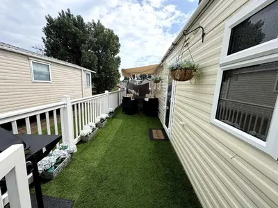 a backyard with green grass next to a house at Modern Caravan With Wifi At Seawick holiday park, Clacton on Sea 8 berth Large Decking in Clacton-on-Sea