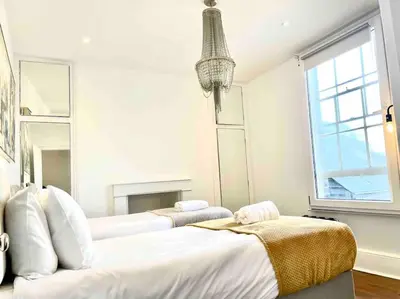 a white bedroom with two beds and a window at EMMANUEL HOUSE LOVELY 1 - BEDROOM APT IN HISTORICAL BUILDING CENTRAL CAMBRIDGE in Cambridge