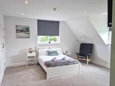 a white bedroom with a bed and a chair at Hyland Apartment by CityNest in Chelmsford