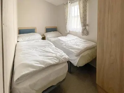 two twin beds in a room with a window at Beautiful 8 Berth Caravan With Decking At Naze Marine Park, Essex Ref 17184P in Walton-on-the-Naze