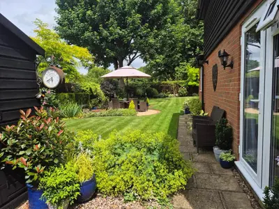 a garden with a clock on the side of a house at Fly By - Duxford close to IWM & Wellcome Genome Campus in Duxford
