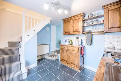 a kitchen with blue walls and wooden cabinets and a staircase at No. 10, The Cottage in Framlingham