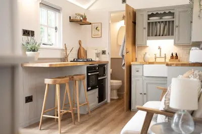 a kitchen with blue cabinets and wooden stools at The Huts At Woodthorpes in Assington