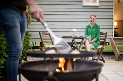 a woman sitting at a table in front of a fire pit at The Huts At Woodthorpes in Assington