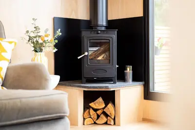 a wood stove in a living room with logs at The Huts At Woodthorpes in Assington