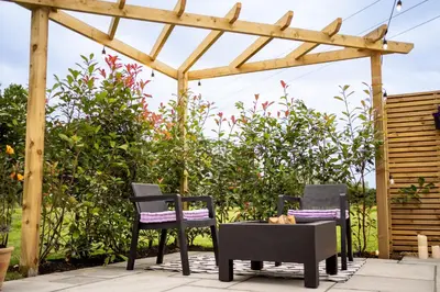 two chairs and a table under a pergola at The Huts At Woodthorpes in Assington
