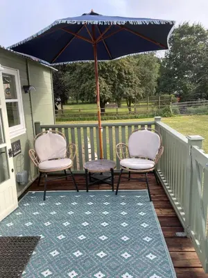 two chairs and an umbrella on a deck at Muffins Meadow Shepherds Hut in Tillingham