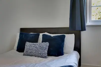 a bed with blue and white pillows and a window at Roman Cottage Chelmsford in Chelmsford