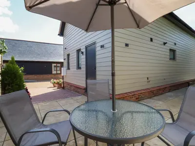 a glass table with chairs and an umbrella on a patio at Wellington Cottage in Ely