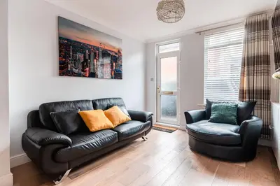 a living room with a black leather couch and a chair at SuffStay in Ipswich