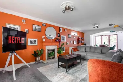 a living room with an orange wall with a tv at The Orange House Langdon Hills in Langdon Hills