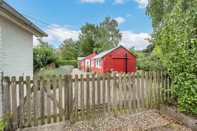 a wooden fence in front of a red house at The Red Shed Entire home for 2 Private garden and parking 2 miles from Bury St Edmunds in Whepstead