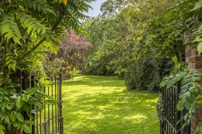 a gate to a garden with green grass and trees at Weavers Mark Cottage in Diss