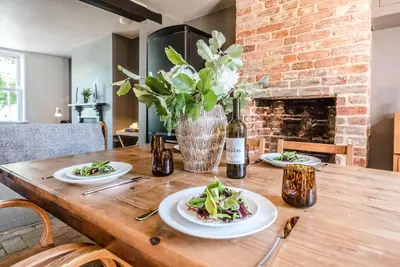 a wooden table with plates of food and a bottle of wine at Key Cottage, Orford in Woodbridge