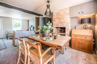 a living room with a wooden table and a brick wall at Key Cottage, Orford in Woodbridge