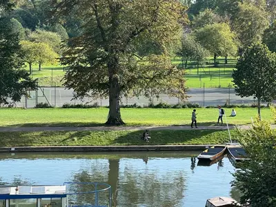 a person walking a dog and a boat in a park at Fig Tree Central Cambridge Apartment Walk to Colleges & River Cam in Cambridge