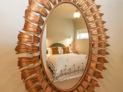 a mirror on a wall with a bed in a room at Rookery Cottage in Saxmundham