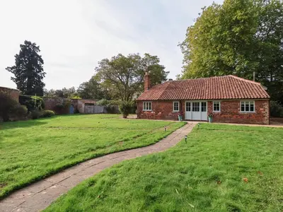a brick house with a grass yard and a driveway at Rookery Cottage in Saxmundham