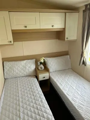 two twin beds in a small room with a night stand at Havah’s in Saint Osyth
