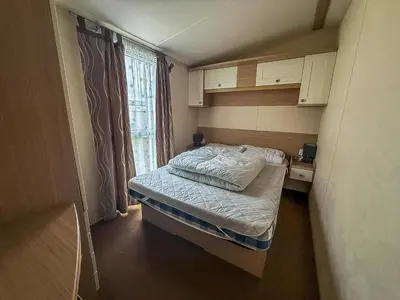 a small bedroom with a bed and a window at Great Caravan On A Family Holiday Park In Essex, Ref 37055G in Clacton-on-Sea