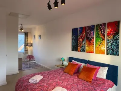 a bedroom with a large bed with colorful pillows at Homely, Cosy & Contemporary 4 BDR house with Garden & Parking 5 mins drive to Addenbrookes & Papworth hospitals & Bio Medical campus in Cambridge