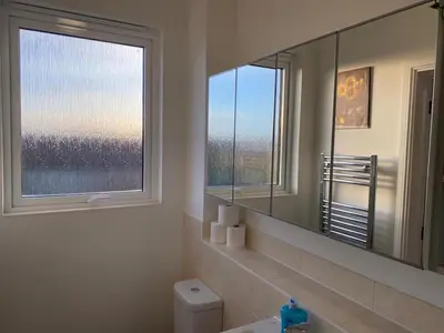 a bathroom with a mirror and a sink and a window at Homely, Cosy & Contemporary 4 BDR house with Garden & Parking 5 mins drive to Addenbrookes & Papworth hospitals & Bio Medical campus in Cambridge