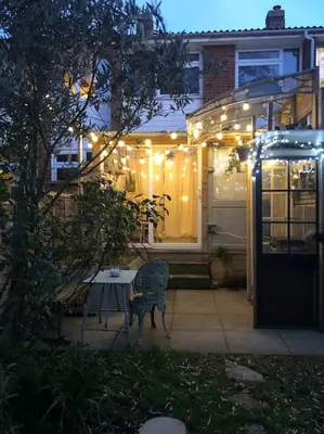 a patio with a table in front of a house with lights at Cosy hideaway with garden sauna in Cambridge in Cambridge