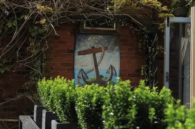 an anchor painted on the side of a building with bushes at The Blue Anchor Feering in Colchester