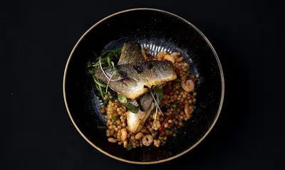 a black plate of food with fish and beans at The Blue Anchor Feering in Colchester