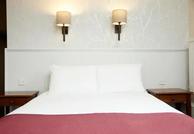 a bedroom with a white bed with two lights on the wall at Lamb Hotel by Greene King Inns in Ely
