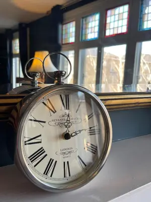 a silver clock sitting in front of a window at Elegant Luxury City Centre Apartment on On Mill Rd - Walk to Station and City Centre in Cambridge