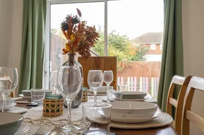 a table with plates and glasses and a vase with flowers at Award Winning Beautiful House in South Cambridge, 14-Min Drive to the City Centre, Free Parking, No Sofabeds, Sleeps 6 in Cambridge