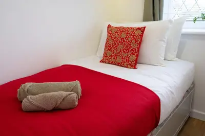 a bed with a red blanket and a stuffed animal on it at Award Winning Beautiful House in South Cambridge, 14-Min Drive to the City Centre, Free Parking, No Sofabeds, Sleeps 6 in Cambridge