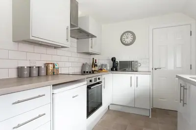 a kitchen with white cabinets and a clock on the wall at Maldon Executive Apartments in Maldon