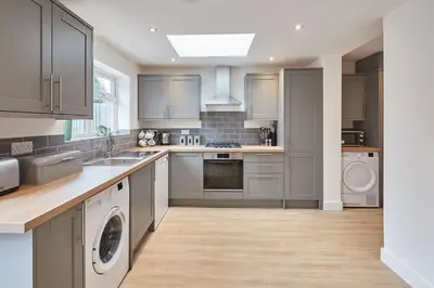 a kitchen with gray cabinets and a washer and dryer at Elfleda Stay - Modern 5 bedroom house with parking in Cambridge